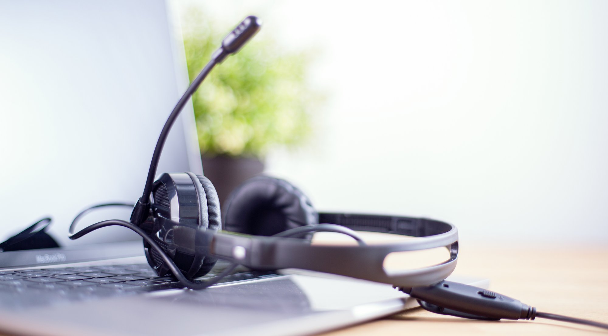 A black headset with a microphone rests on the keyboard of an open laptop, suggesting a workspace focused on AI for private equity, with a green plant blurred in the background on a wooden desk.